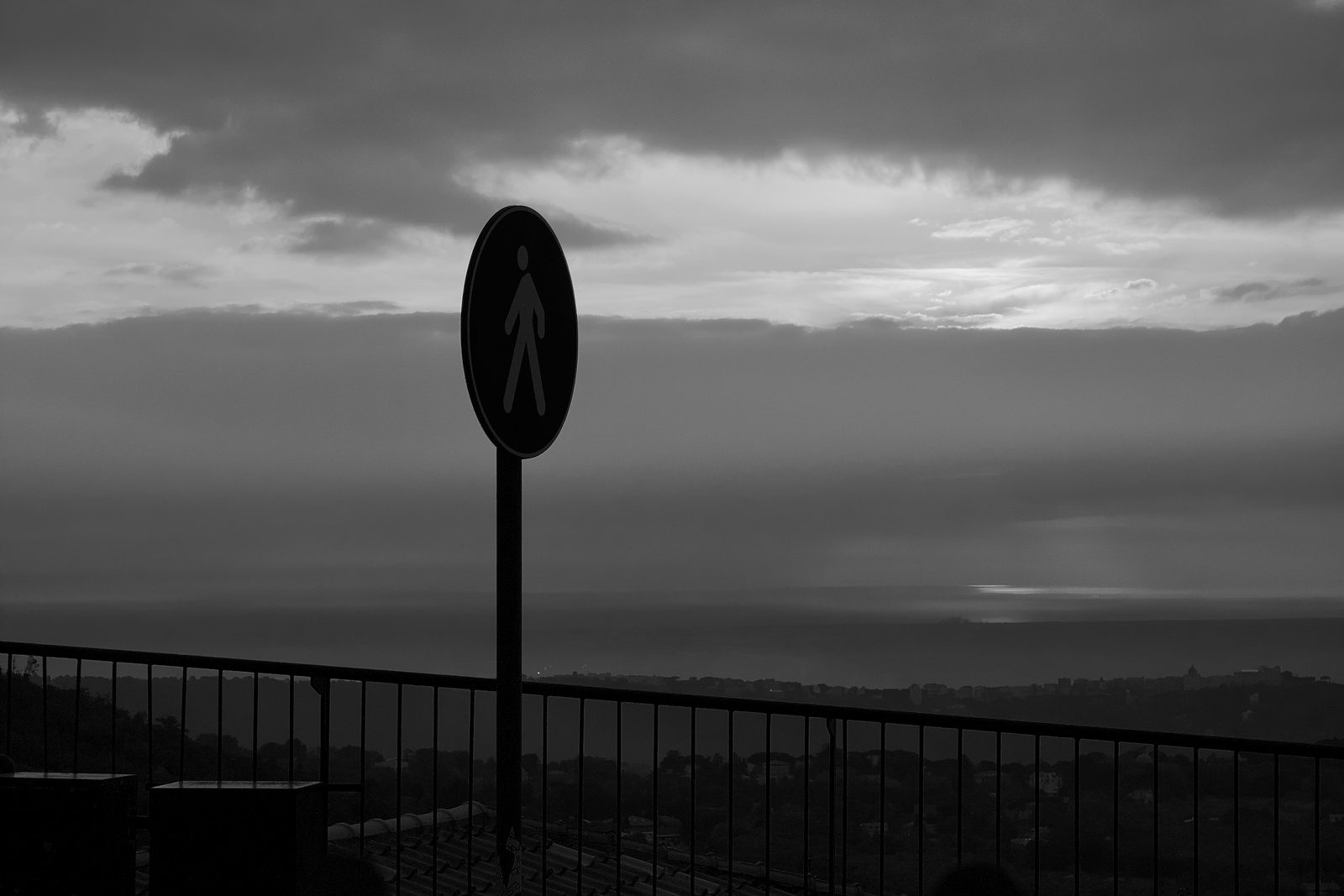 A road sign silhouetted against a heavy sky at dusk, in black and white.