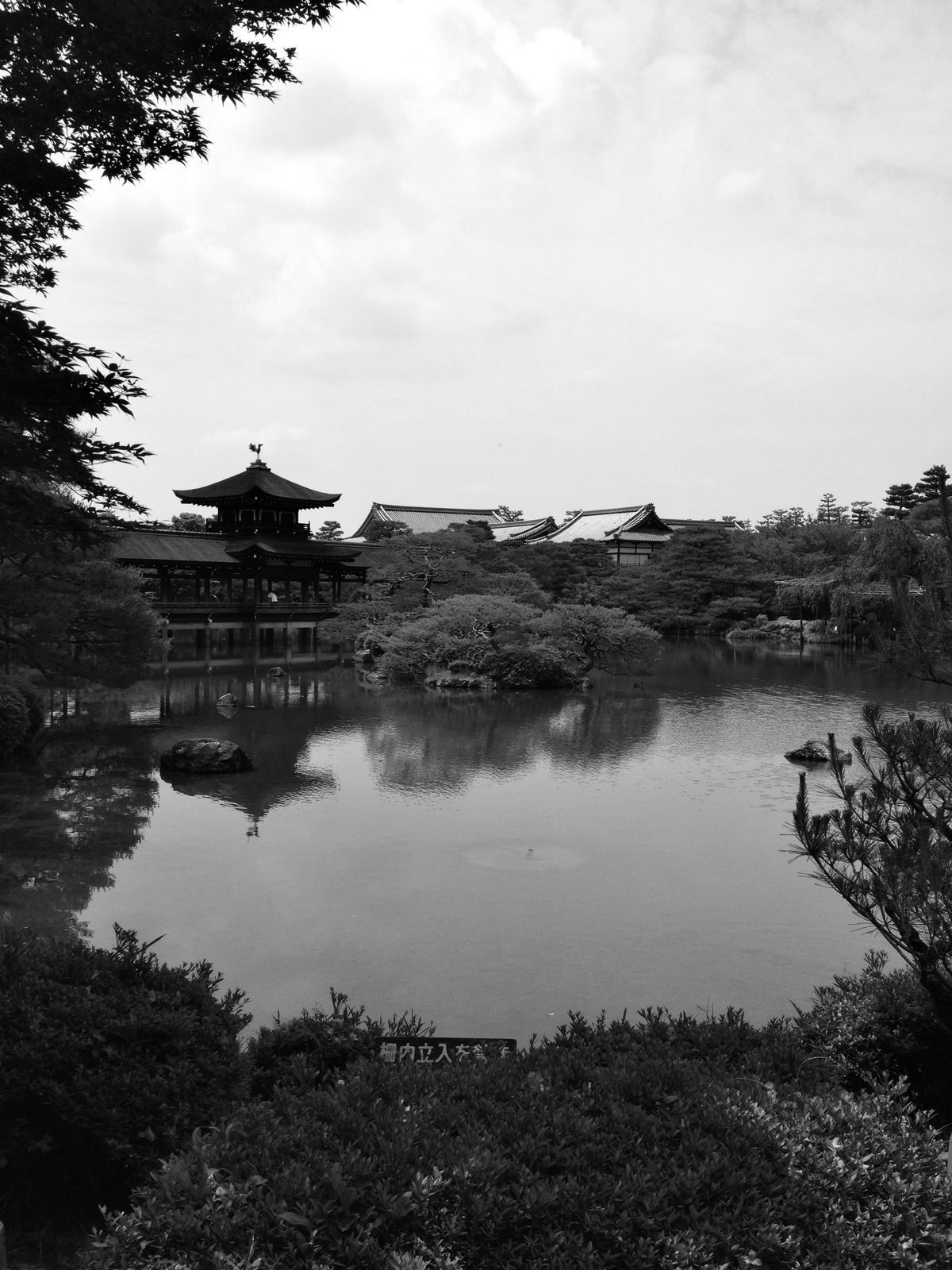 A pagoda across a still pond, reflected in the water, in black and white.