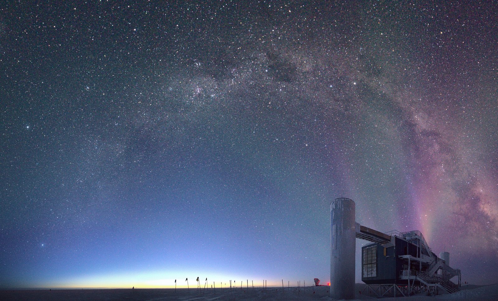 The IceCube Laboratory at the South Pole under a green aurora, with the Milky Way overhead.